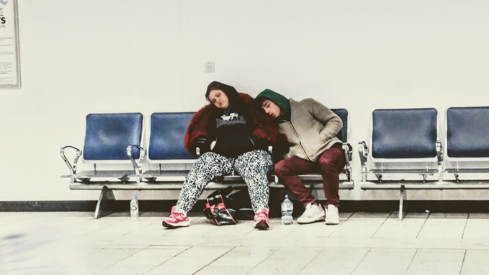 A woman and a boy sleeping on a the aligned chairs of an airport